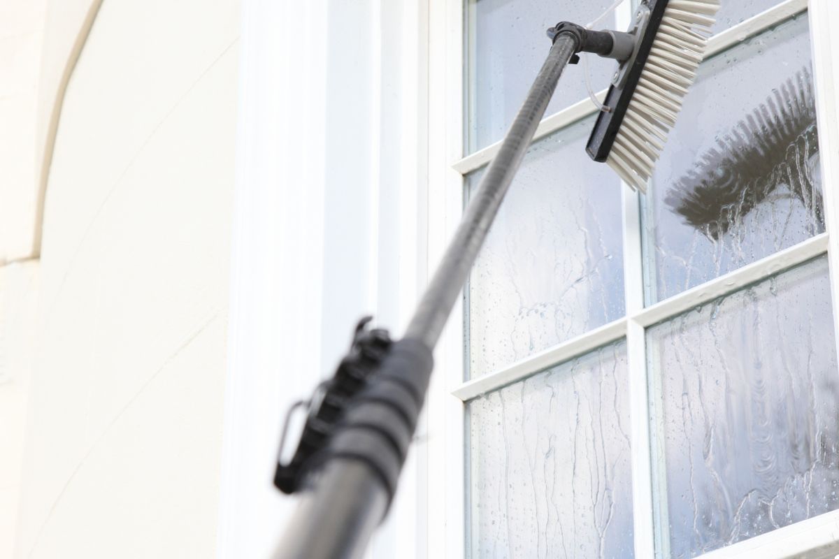 A person uses a window cleaning brush to effectively clean a large window, ensuring a clear and spotless surface.