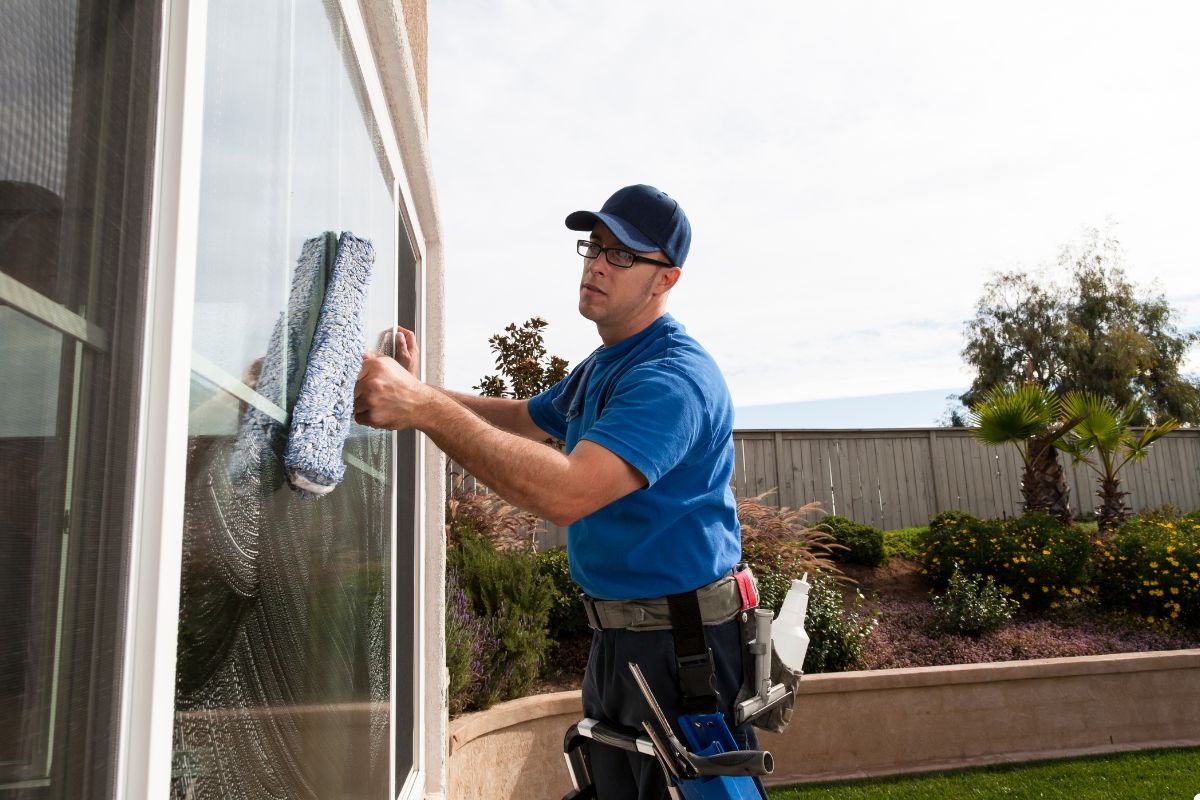 A man dressed in a blue shirt is diligently cleaning windows with a blue cloth, enhancing the cleanliness of the glass.