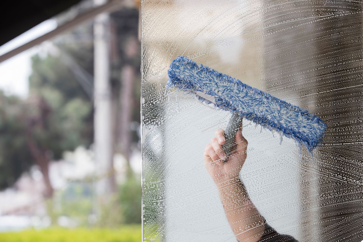 Individual cleaning a window with a blue brush, focusing on achieving a streak-free finish.