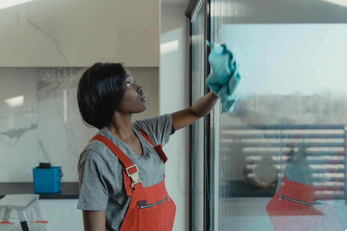 A woman in an apron diligently cleans a window, showcasing her commitment to maintaining a tidy environment.