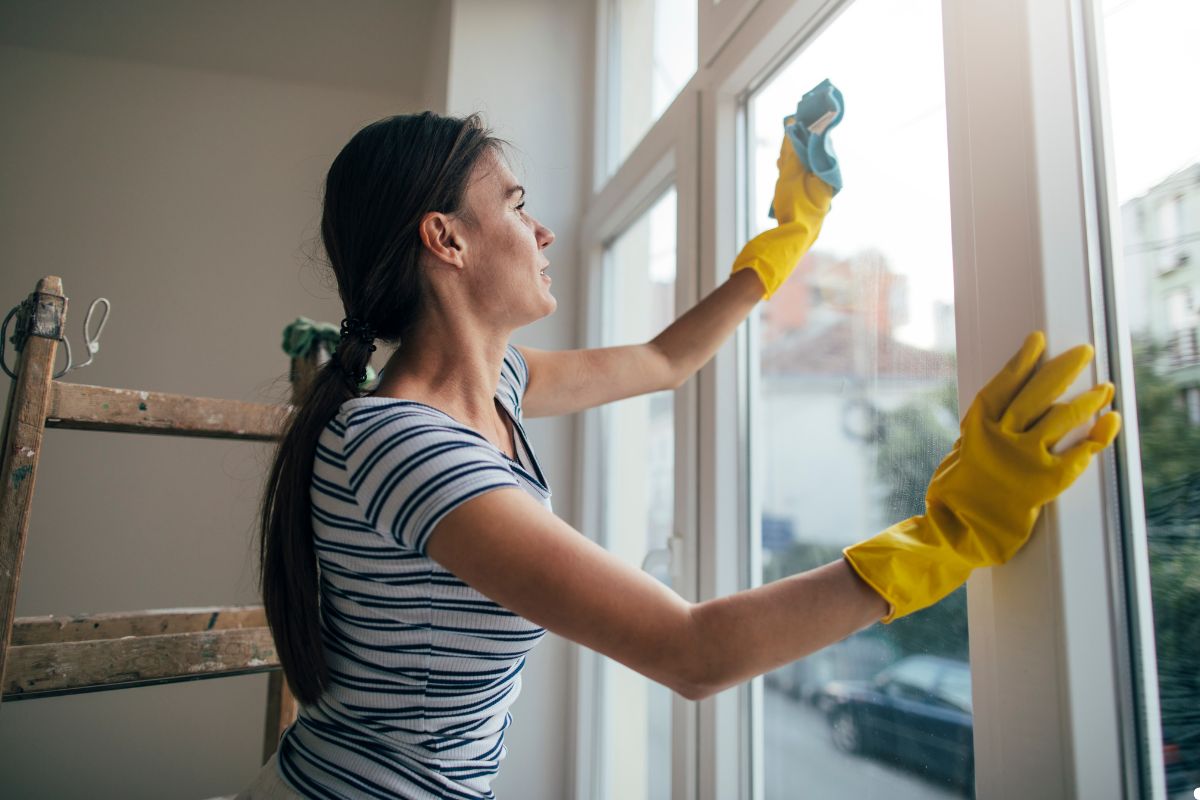 A woman wearing gloves cleans a window with a mop, focusing on removing dirt and streaks for a clear view.
